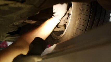 Auto mechanic uses hydraulic play detector to inspect car suspension, steering systems at vehicle service station. Expert checks undercarriage parts for safety, efficiency. Car maintenance.