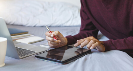 Asian man with tablet and laptop on the bed. freelance work part time on holiday and ckecking work...