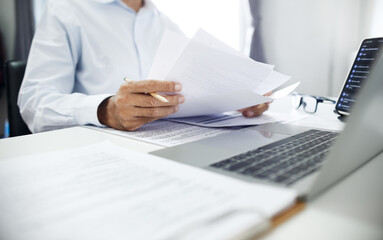 Business consultant holding pencil reviewing documents and contact customer via laptop to give advice about business contracts and various important documents before investing in business