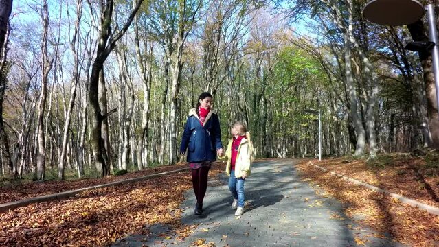 mother and daughter walk by the hand, kiss, walk through the autumn forest