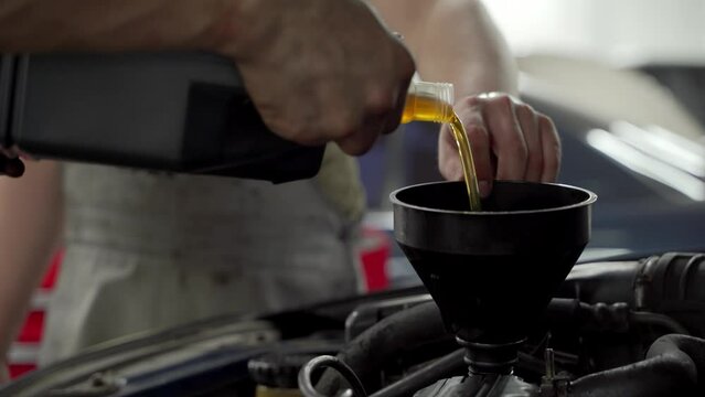 Auto technician pours new motor oil into car engine, performs routine maintenance. Professional service at auto shop. Vehicle upkeep, changing lubricant for better performance, efficiency.