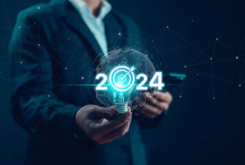Businessman shows business goals for 2024 on a 2024 light bulb. Analytical plans business growth in...