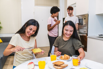 Friends smiling as they spread butter on toast during a homemade breakfast in a modern kitchen setting