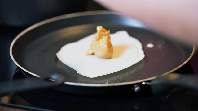 Closeup of making steaming hot crepe layer on a cast iron pan. A thin pancake made with rice flour dough and condensed milk stuffing. Thin batter being spread and cooked for making 'Pithe' and 'dosa'
