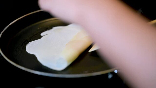 Closeup of making steaming hot crepe layer on a cast iron pan. A thin pancake made with rice flour dough and condensed milk stuffing. Thin batter being spread and cooked for making 'Pithe' and 'dosa'