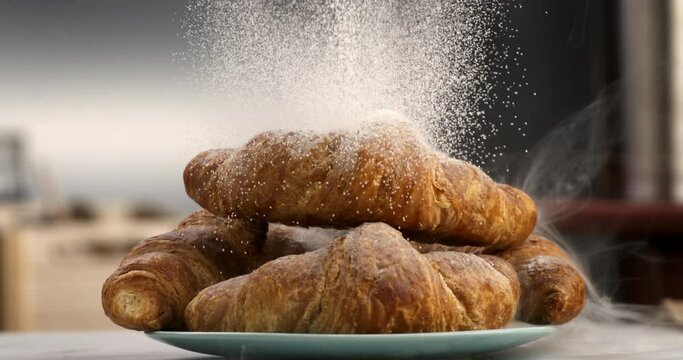 Super slow motion close up of sweet icing sugar powder is falling on sweet delicious dessert French croissant in traditional artisan bakery kitchen at 1000 fps.