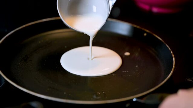 Closeup of making steaming hot crepe layer on a cast iron pan. A thin pancake made with rice flour dough and condensed milk stuffing. Thin batter being spread and cooked for making 'Pithe' and 'dosa'
