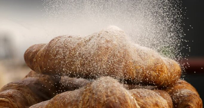 Super slow motion macro of sweet icing sugar powder is falling on sweet delicious dessert french croissant in traditional artisan bakery kitchen at 1000 fps.