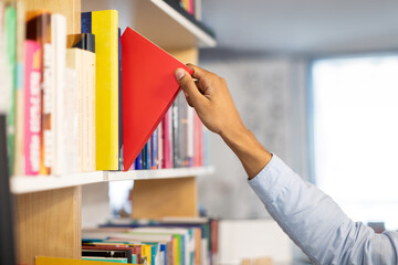 Closeup of black male student's hand as he taking book from shelf in library, capturing the focused moment of tactile engagement with literature