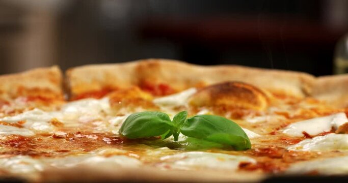 Super slow motion macro of fresh green basil leaf is falling on traditional italian dish of pizza margherita with tomato sauce and mozzarella cheese in rustic restaurant kitchen at 1000 fps.