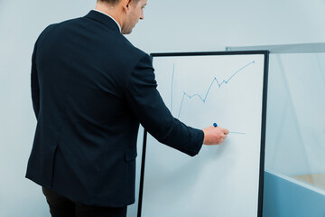 Closeup of smart male leader drawing increasing graph at business meeting room while standing at...
