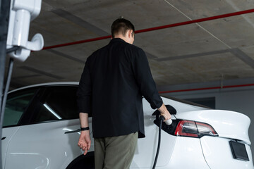 Young man travel with EV electric car to shopping center parking lot charging in downtown city...