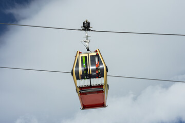 Close-up of cable car or ski lift cabin with alpine skis moving against the background of cloudy...