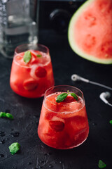 Two glasses of watermelon and strawberry cocktail on dark concrete background