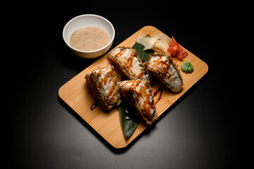 Top view of sushi rolls tempura sandwich with unagi sauce on wooden board with wasabi and ginger