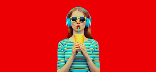Fashion portrait of stylish young woman listening to music with headphones drinking fresh juice...