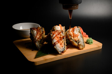 Close-up of a sushi roll, a tempura sandwich with wasabi and ginger, finished with brown sauce from a bottle