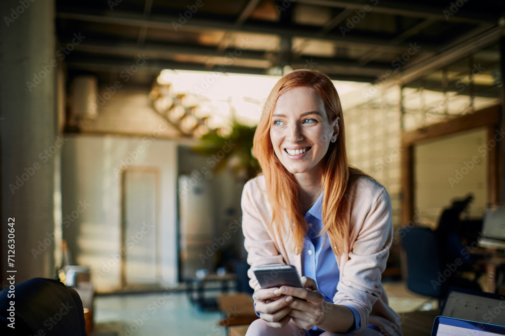 Wall mural Smiling young business woman using smartphone in modern office