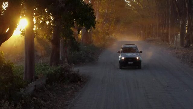 automovil viajando por un polvoriento camino rural en un atardecer con intensos rayos de luz