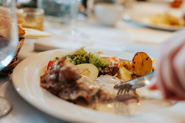 A person eating grilled meat with vegetables in restaurant - close-up on hands and plate