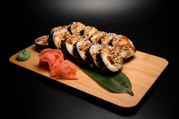 Side view of sushi rolls covered with brown sauce and sprinkled with sesame seeds