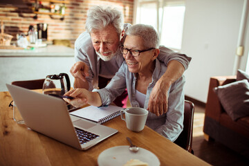 Smiling senior couple using laptop together at home