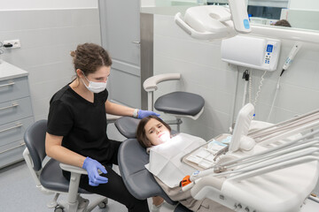 A pediatric dentist examines an anxious child who has come to an appointment for the first time. Medical examination of a child at a pediatric dentist. Prevention of diseases of baby teeth in children