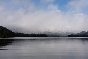 andscape with snow-capped mountains shrouded by clouds and reflected in the lake