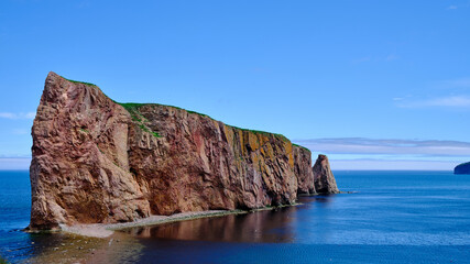 Obraz premium The beautiful colors, natural arch and shape of famous Perce Rock on the Gaspe Peninsula in Quebec Canada at sunset with it's red-pinkish colors from the shores of Perce Village
