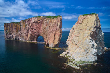 Naklejka premium The beautiful colors, natural arch and shape of famous Perce Rock on the Gaspe Peninsula in Quebec Canada with it's red-pinkish colors from an aerial drone image