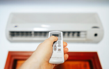 Hand holding remote control in front of the air conditioner.