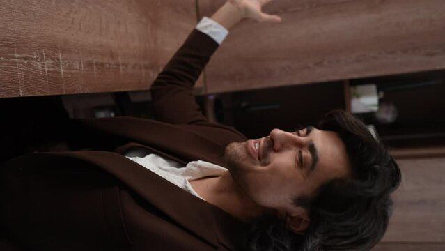 POV vertical video cheerful businessman in formal suit talking on video call, bragging about office using smartphone sitting in desk. Successful male entrepreneur communicates looking at camera.