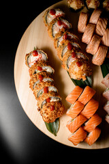 Top view of half a set of sushi rolls on a round wooden board: two sliced fried rolls in batter