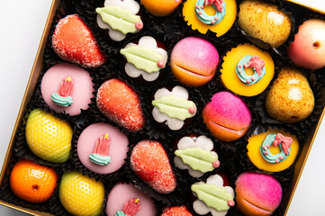 Box of rainbow marzipan sweets in form of different fruits and cakes