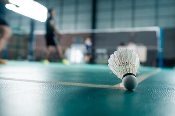 Badminton shuttlecock landing on the line of the court with blurred people playing in the background.