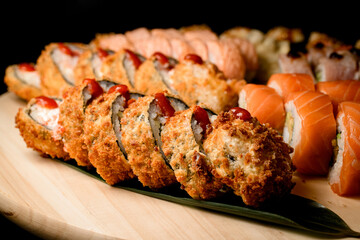 Focus on the foreground of fried tempura sushi rolls in batter with drops of sauce on top
