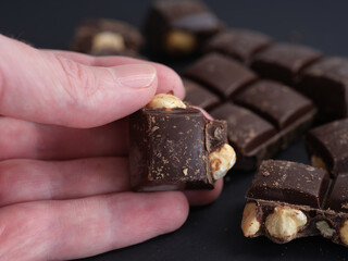 A man holding a piece of dark chocolate with hazelnuts in his hand. Close up.