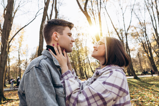 Heterosexual caucasian young loving couple walking outside in the city park in sunny weather, hugging smiling kissing laughing spending time together. Autumn, fall season, orange yellow red leaves

