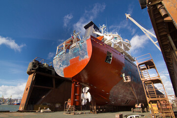 Commercial vessel in dry dock for maintenance. Ship undergoes hull painting and repairs. Maritime,...