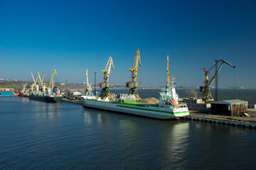 Cargo ship docked at international port, cranes load containers for global trade. Clear sky, calm...