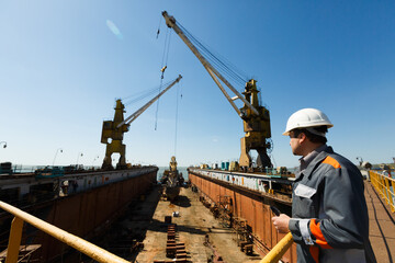Professional overseeing extensive shipbuilding process, massive cranes erect vessel in dry dock...
