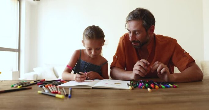 Caring mature father and little 6s daughter painting pictures with colorful felt-tips, sit together at table in living room, engaged in creative activity. Kids development, family pastime and hobby