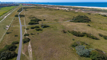 Top view of the beach kijkduin and sea. Flight over fields with green grass and buildings on the seashore. Roofs of houses in the background. View from a quadrocopter fields near the North Sea - 712663247