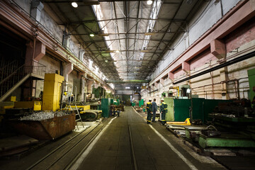 Industrial workers operate heavy machinery in metalworking factory. Engineers in safety gear work...