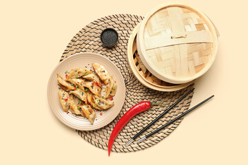 Plate with tasty Chinese jiaozi, red chili pepper and bamboo steamer on beige background