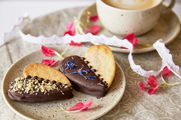 Aesthetic vegan cookies in heart shape among flowers and cup of coffee. Romantic holiday food background
