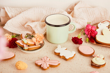 Mug of milk among sweet decorated cookies and flowers. Springtime floral aesthetic background.