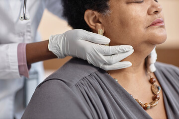 Close up shot of unrecognizable doctors hands in gloves touching senior woman patients neck during check up in clinic
