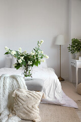 Vase with blooming jasmine flowers on bedside bench in interior of light bedroom