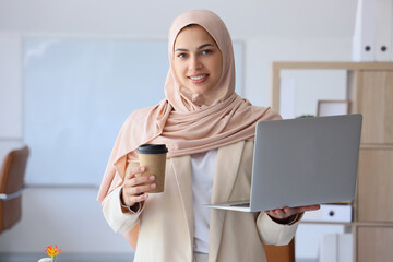 Pretty Muslim female programmer with laptop and cup of coffee in office